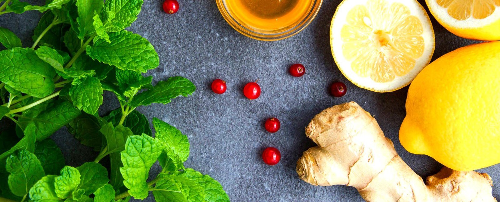 Fresh mint, honey, lemon, ginger and berries on a stone surface